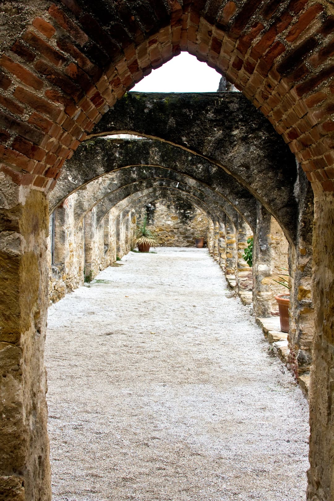 A long gravel walkway framed by a series of historic brick and stone arches.