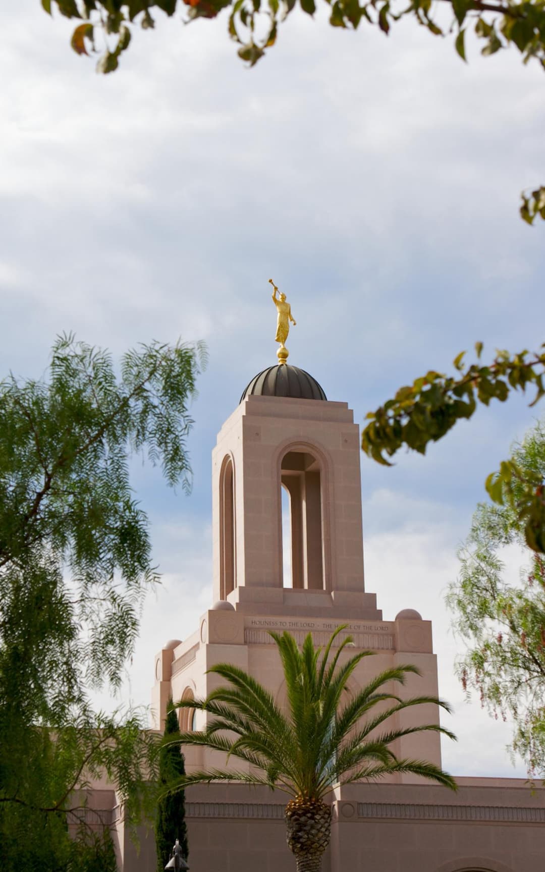 Newport Beach Temple tower with Angel Moroni and inscription, framed by trees.