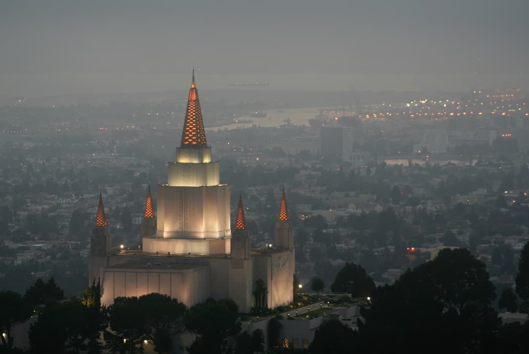 Oakland Temple exterior at dusk with city lights visible through haze.