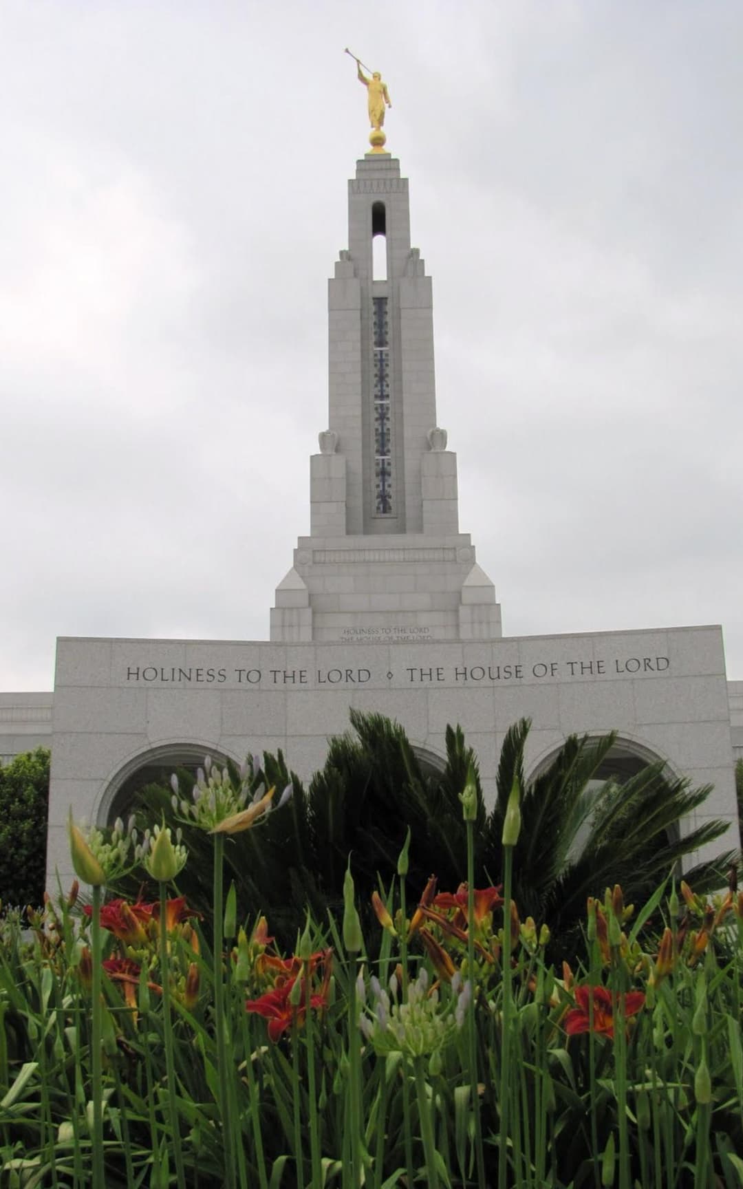 Low-angle view of the temple spire and front entrance framed by garden flowers.