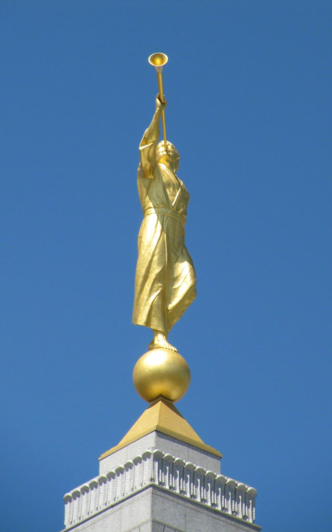 The golden Angel Moroni statue atop the spire against a clear blue sky.