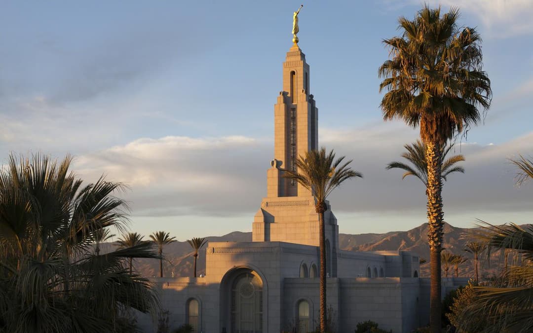 The Redlands California Temple spire framed by palm trees at sunset.