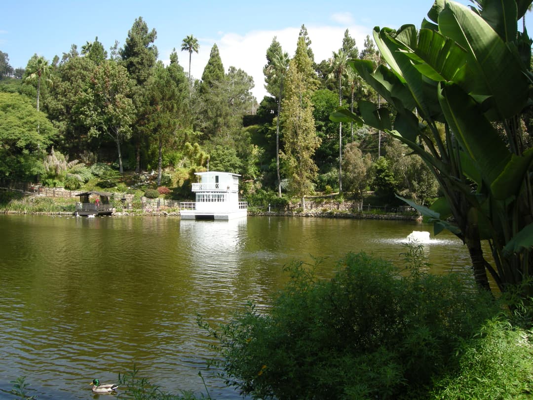 Wide view of the spring-fed lake with the white houseboat and lush gardens.