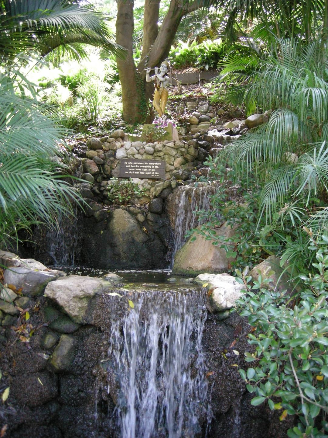 Cascading stone waterfall with a Krishna statue in the meditation gardens.