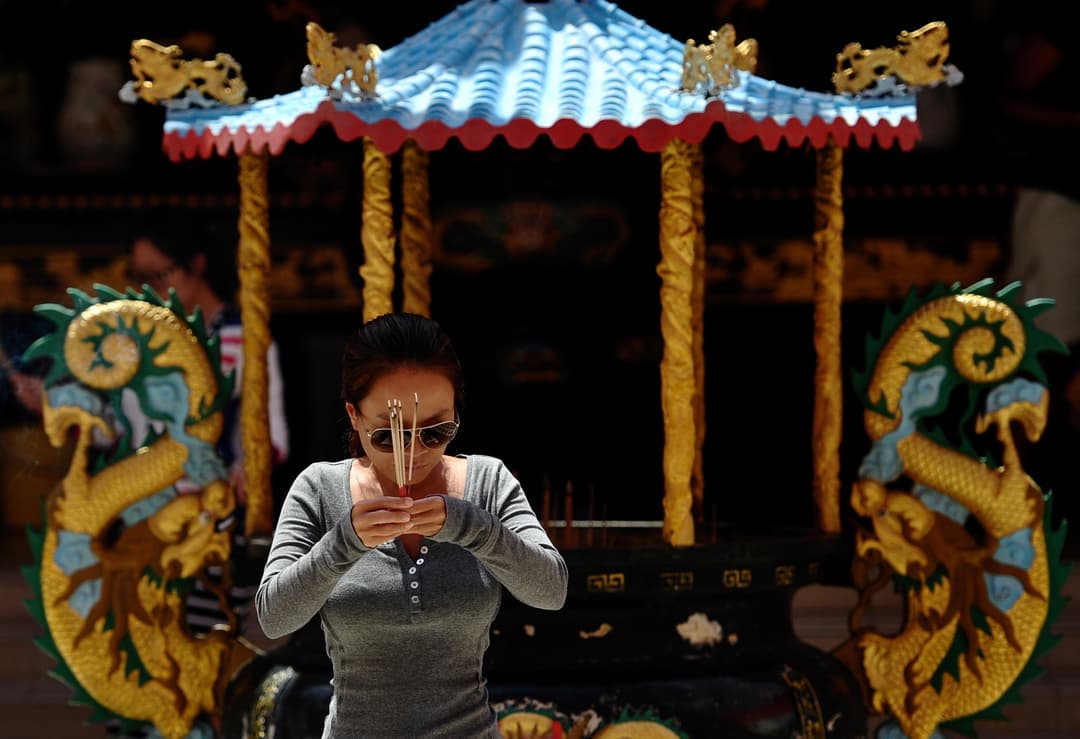 A worshipper holding incense before an ornate shrine at Tien Hau Temple.
