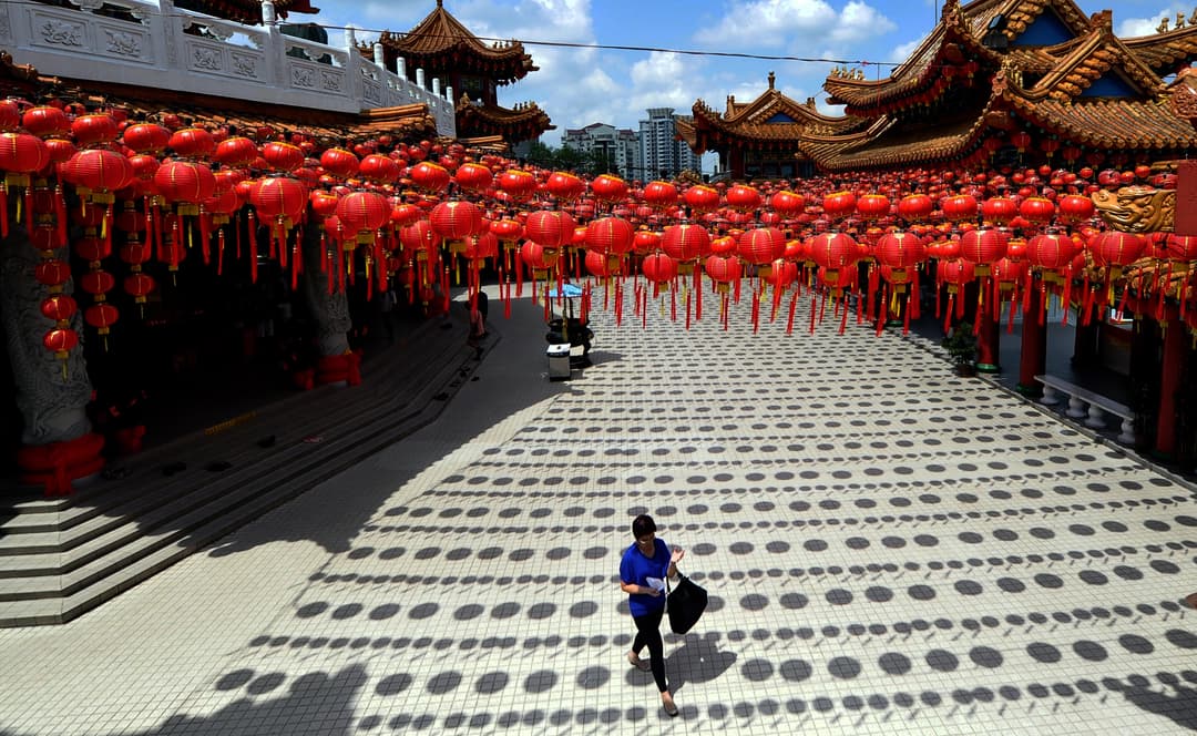 Red lanterns casting circular shadows across a sunlit temple courtyard.