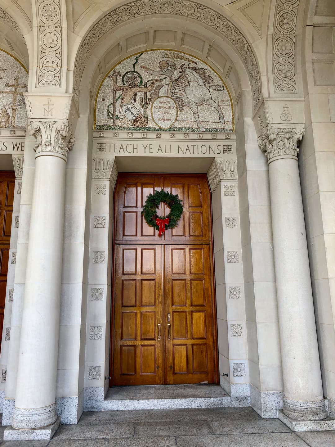 Exterior doorway with "Teach Ye All Nations" inscription and mosaic tympanum.