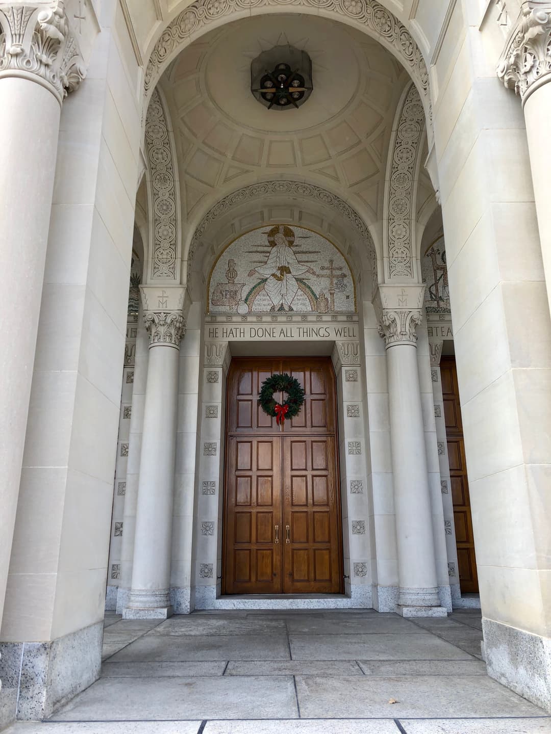 Arched portico entrance with a mosaic above the wooden doors.
