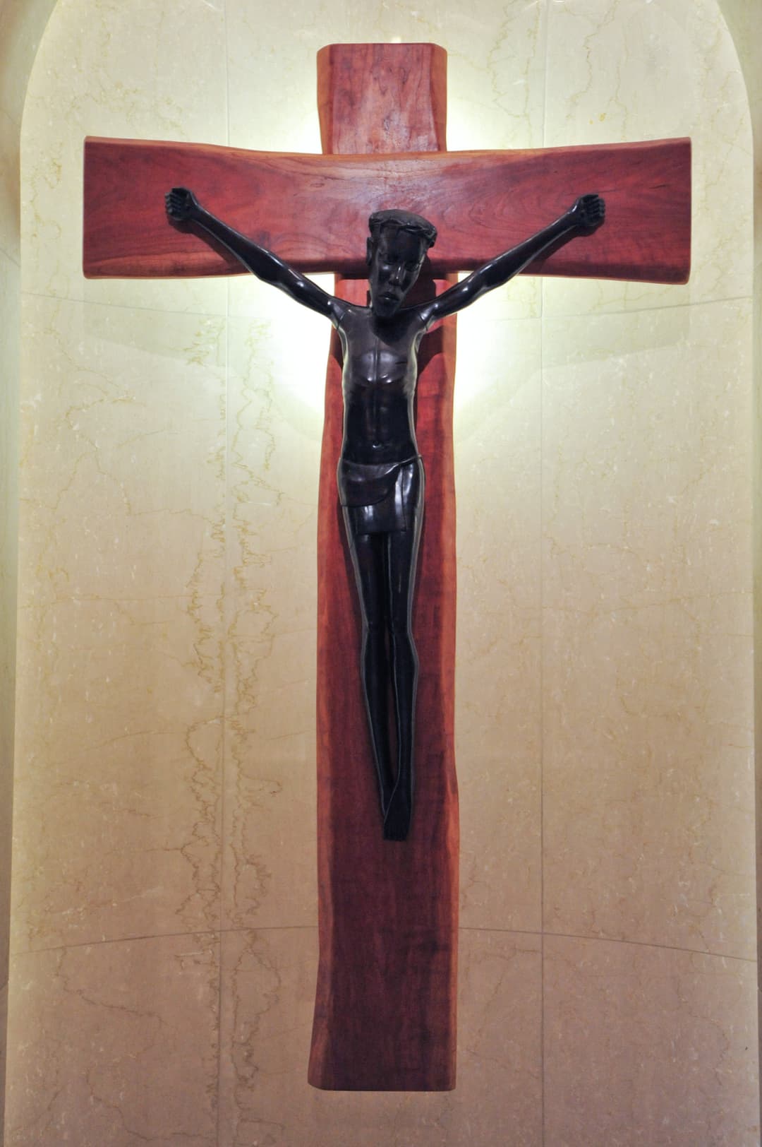 Interior detail of a dark wooden crucifix set against a marble wall.