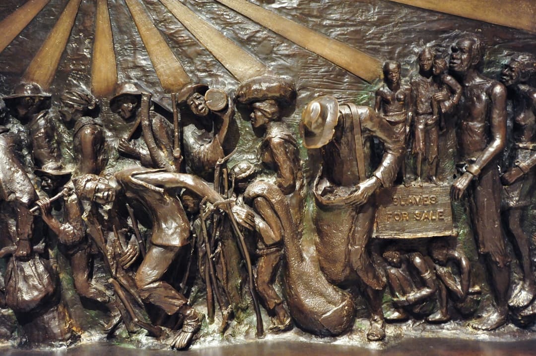 Detail of a bronze relief panel depicting enslaved people for sale.