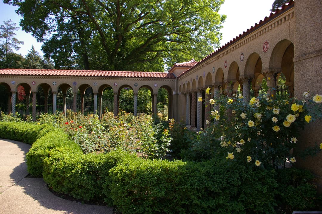 View of the arcaded Rosary Portico and rose garden in daylight.