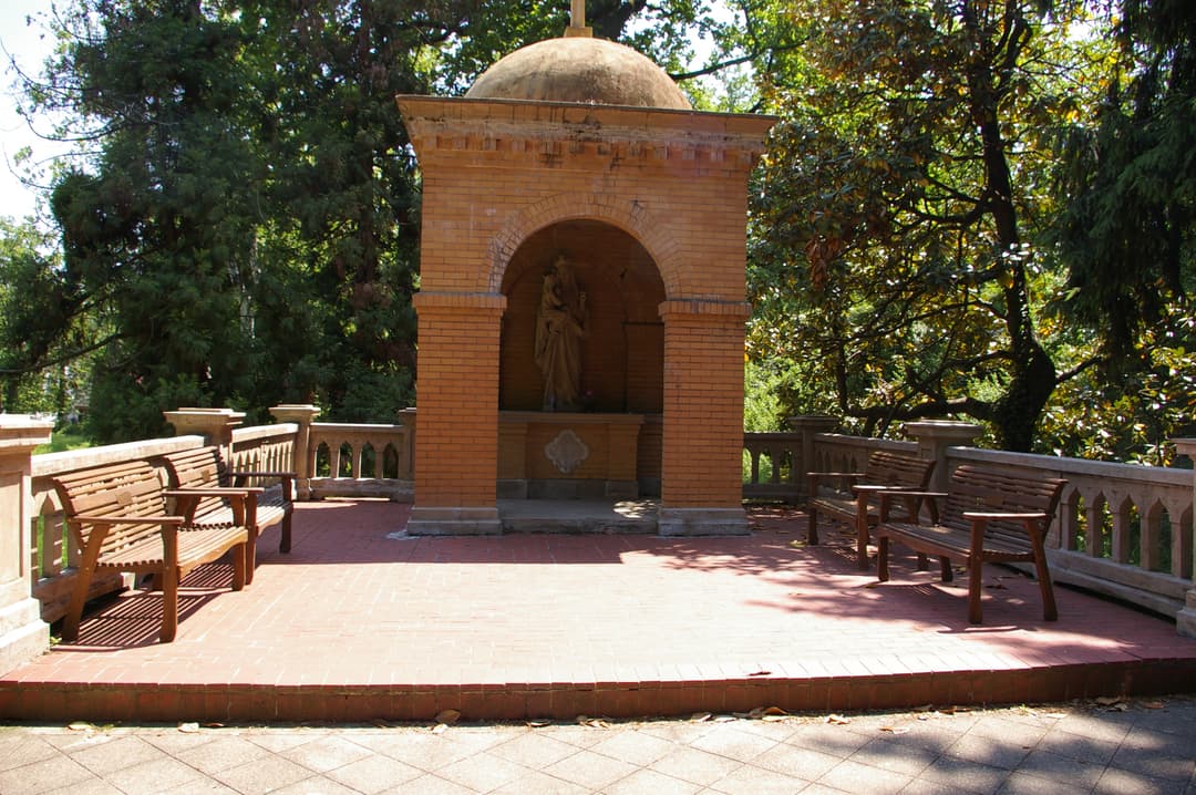 Domed brick shrine on a paved terrace with benches in the monastery gardens.
