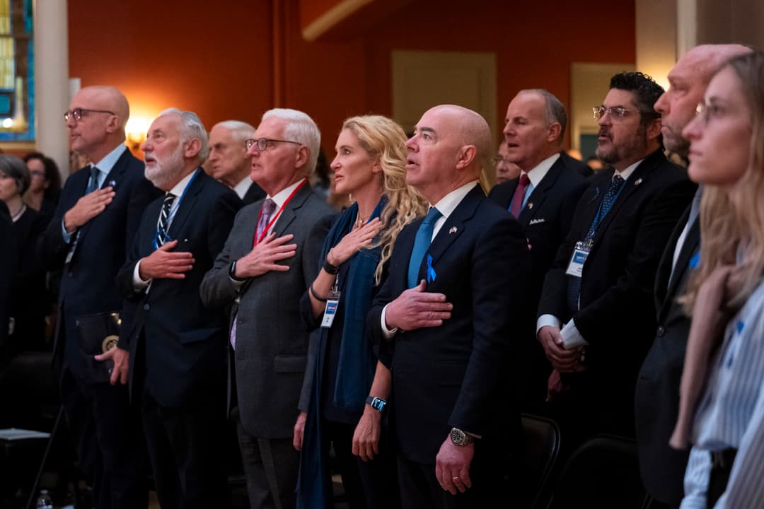 Interior view of attendees standing with hands over their hearts at an event.