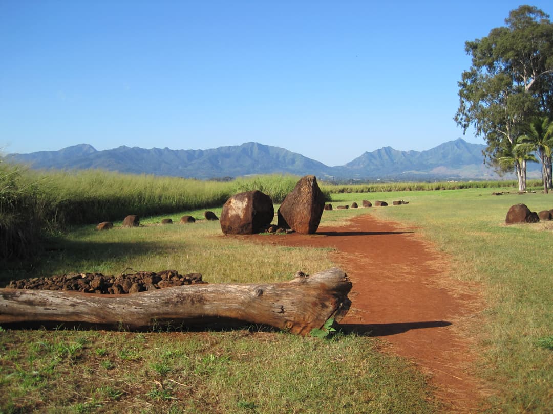 Wide grounds view of Kūkaniloko Birthstones against distant mountains.