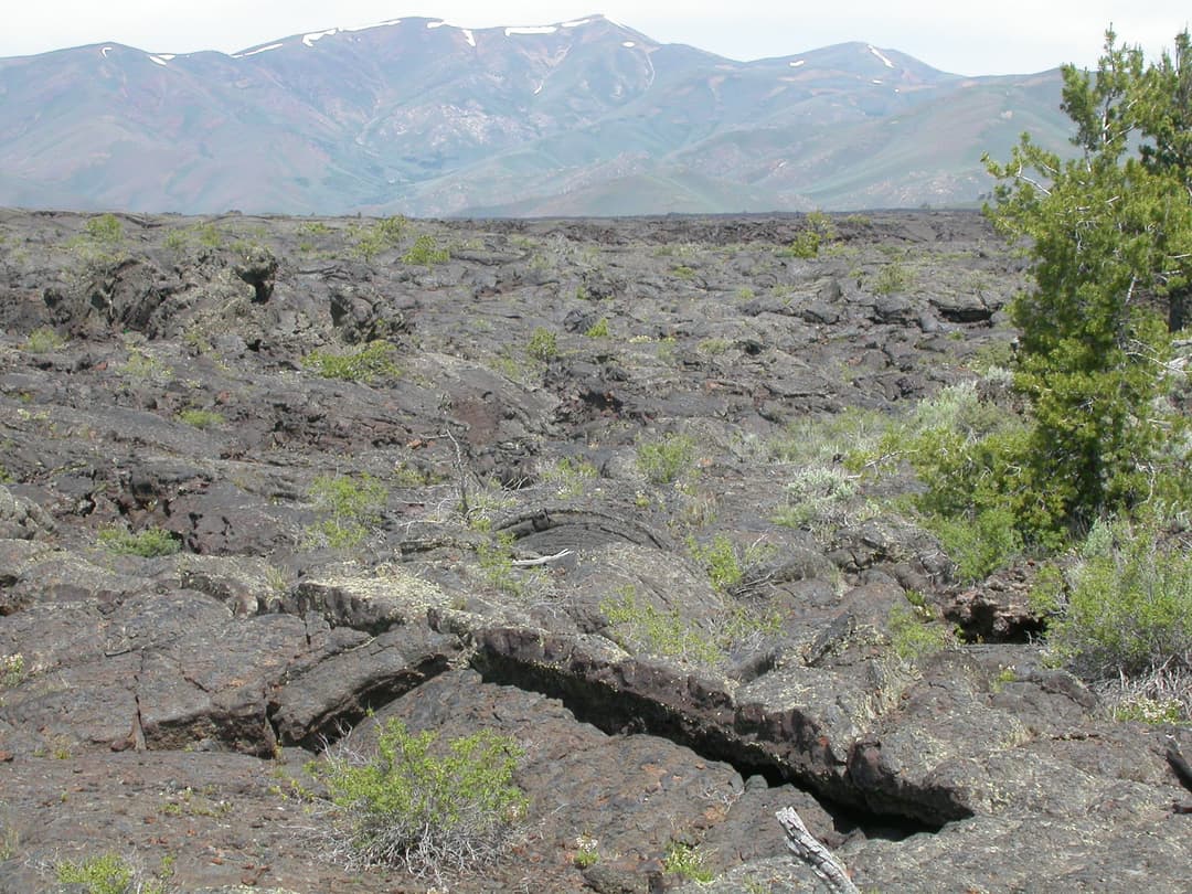 Wide view of rugged basalt lava fields and distant mountains under daylight.