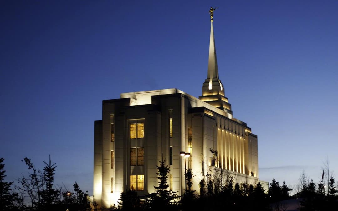 Rexburg Idaho Temple at twilight, illuminated, with Angel Moroni spire.