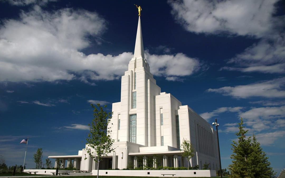 Rexburg Idaho Temple exterior, spire with Angel Moroni under a cloudy blue sky.