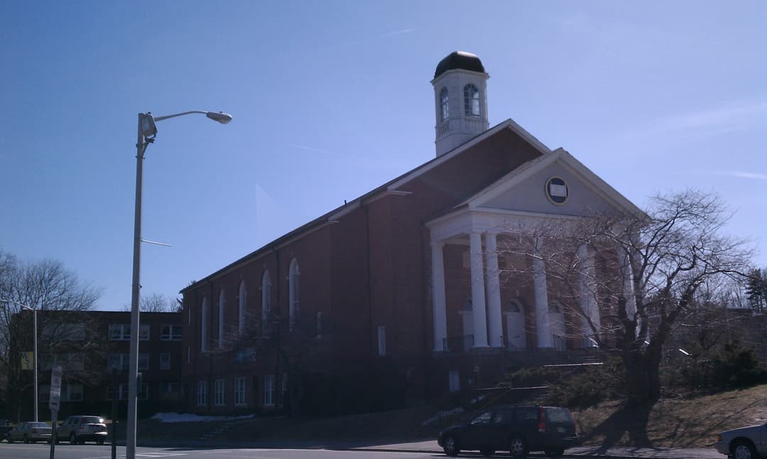 Angled exterior view of the brick building with columned portico and cupola.