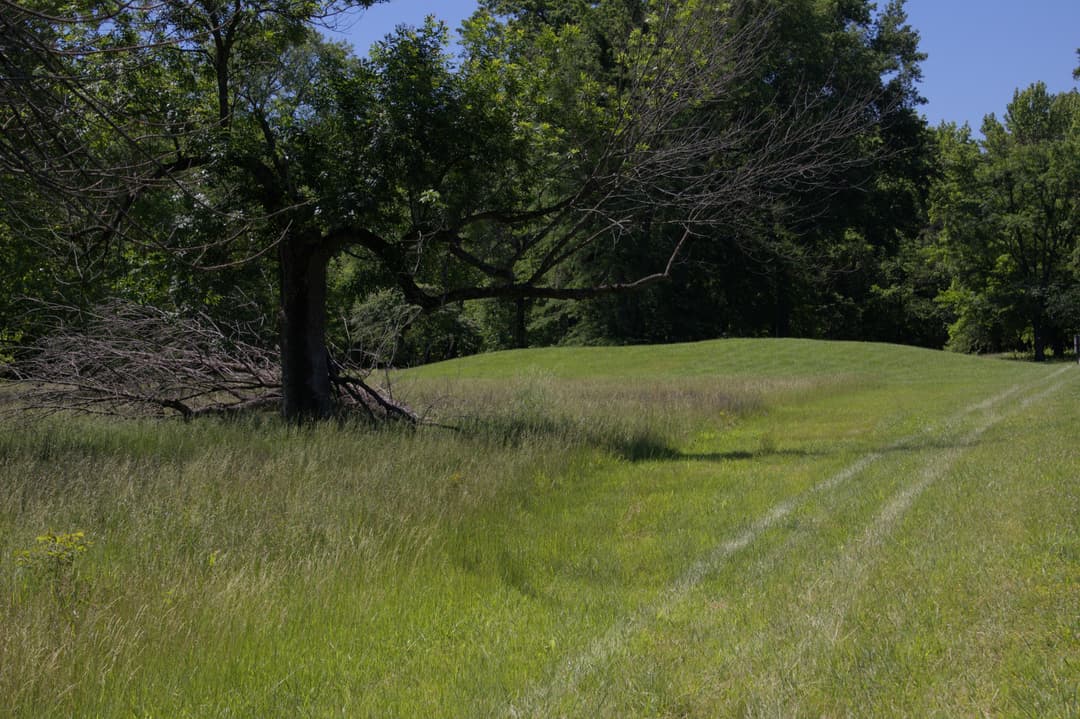 Daylight view of an earthen mound across grassy park grounds.