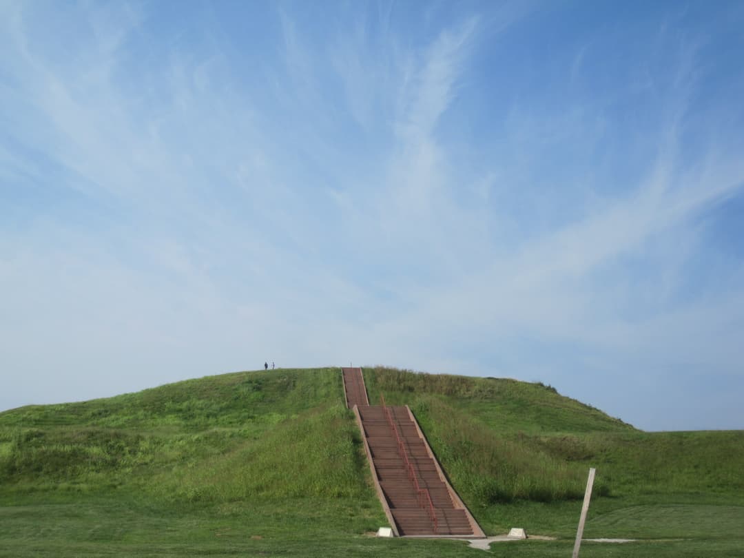 Ground-level view of the wooden staircase ascending the grassy earthen mound.