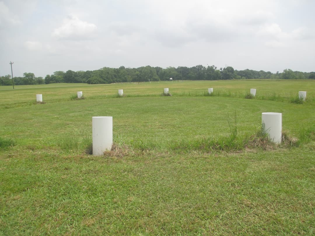 White post markers defining a post circle in an open grassy field.
