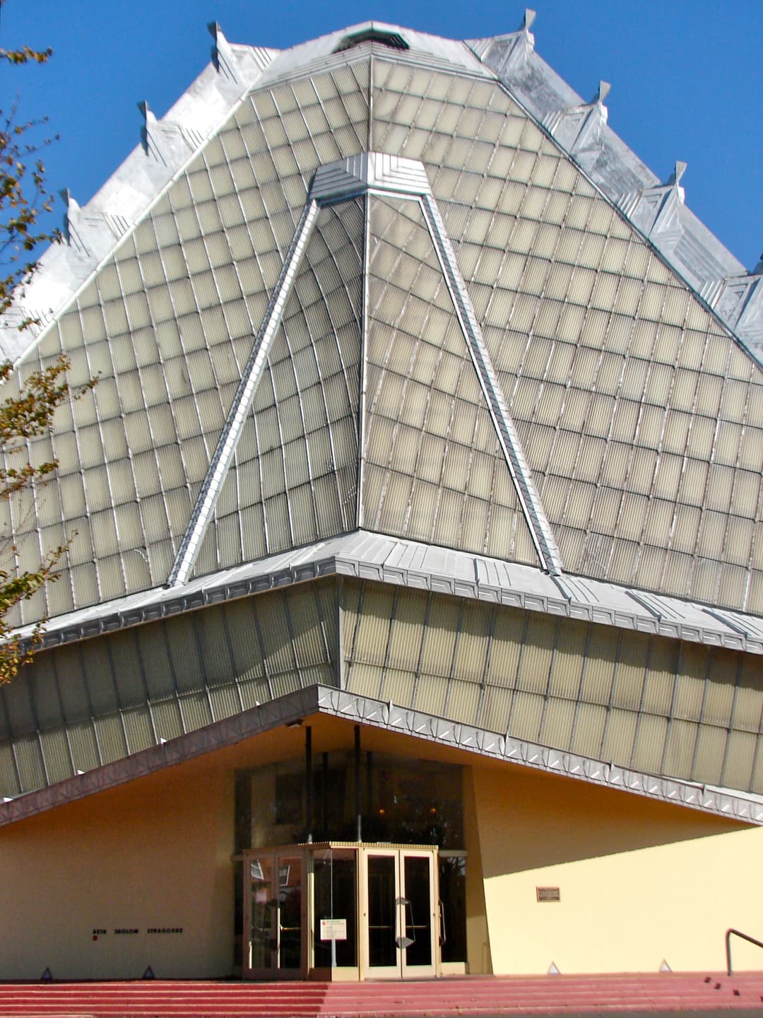 Front entrance and towering translucent pyramidal roof in daylight.