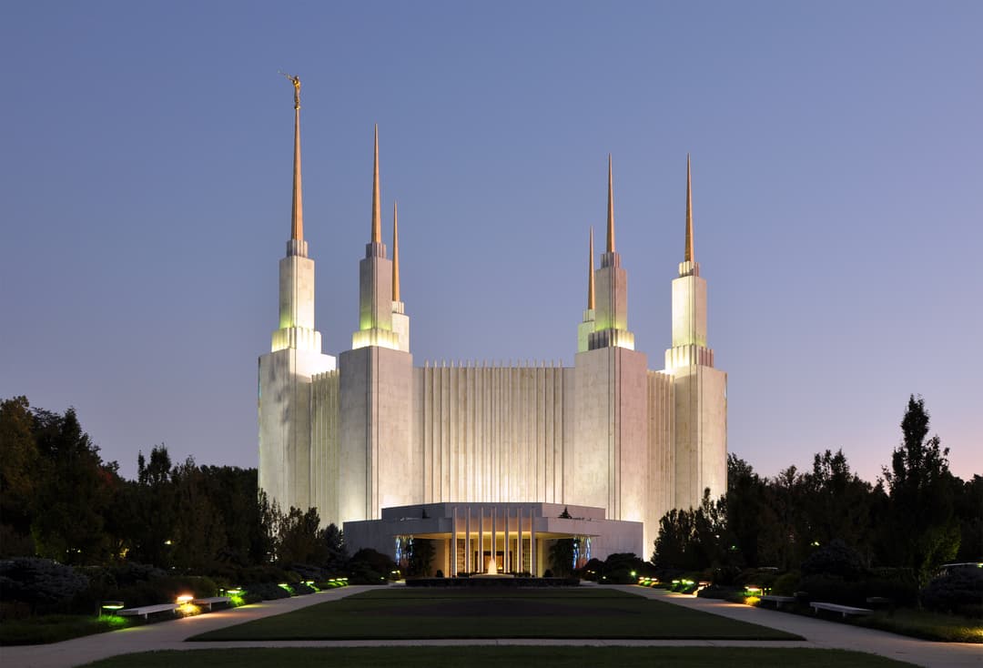 Washington D.C. Temple at dusk, wide shot of six spires and illuminated grounds.