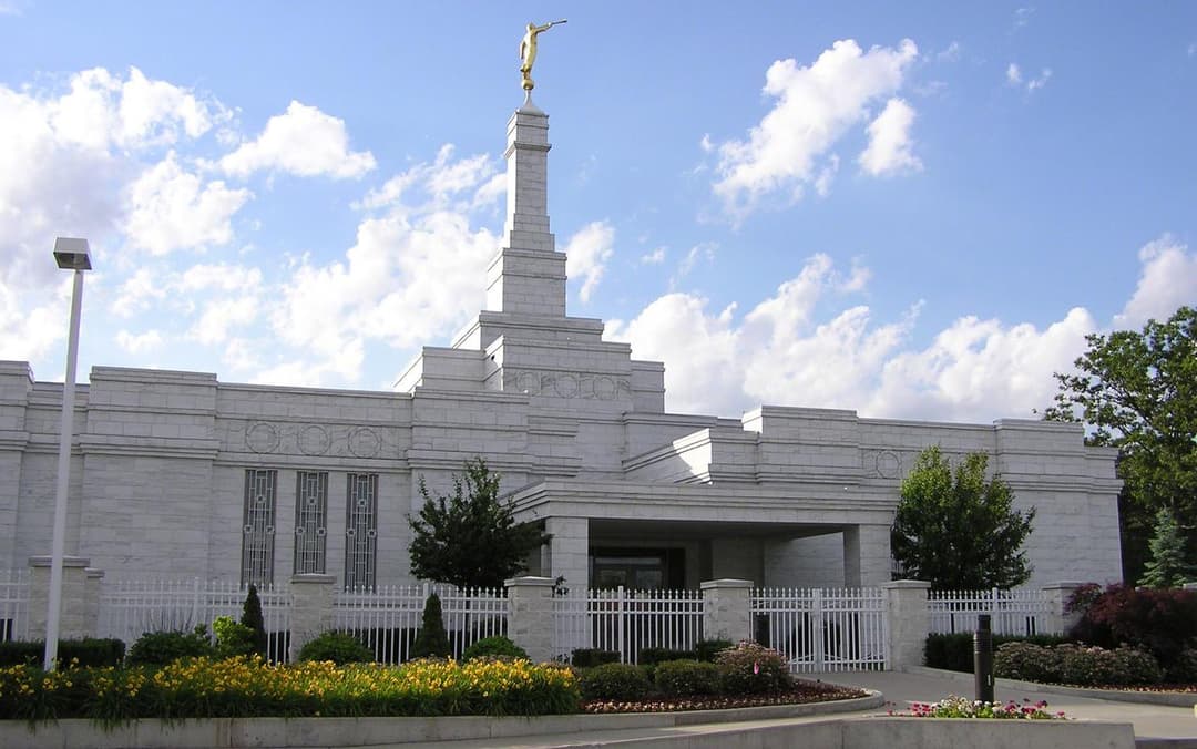 Detroit Michigan Temple exterior, daytime, with spire, Angel Moroni, and grounds.