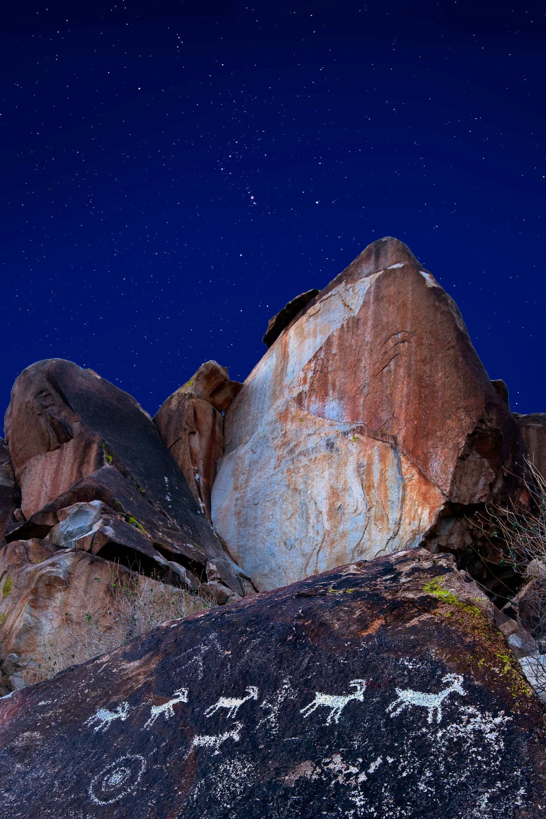 Ancient petroglyphs on granite rocks beneath a starry night sky.
