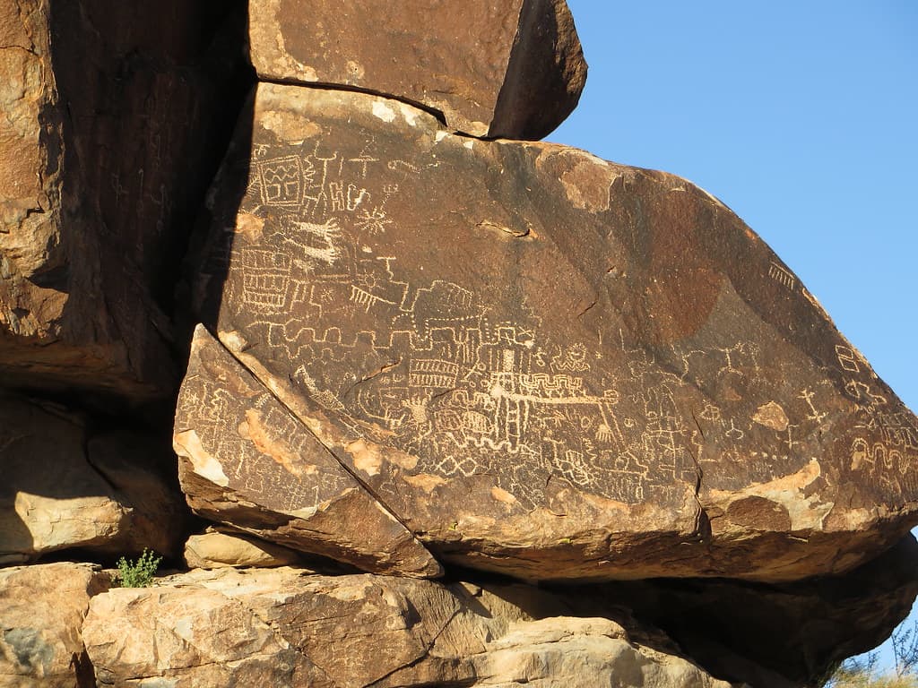 Intricate ancient petroglyphs etched into a sunlit granite boulder panel.
