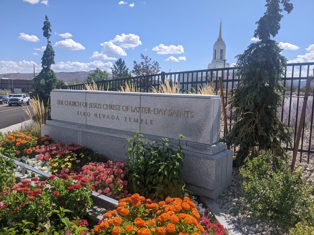 Elko Nevada Temple sign, vibrant gardens, and spire on a sunny day.