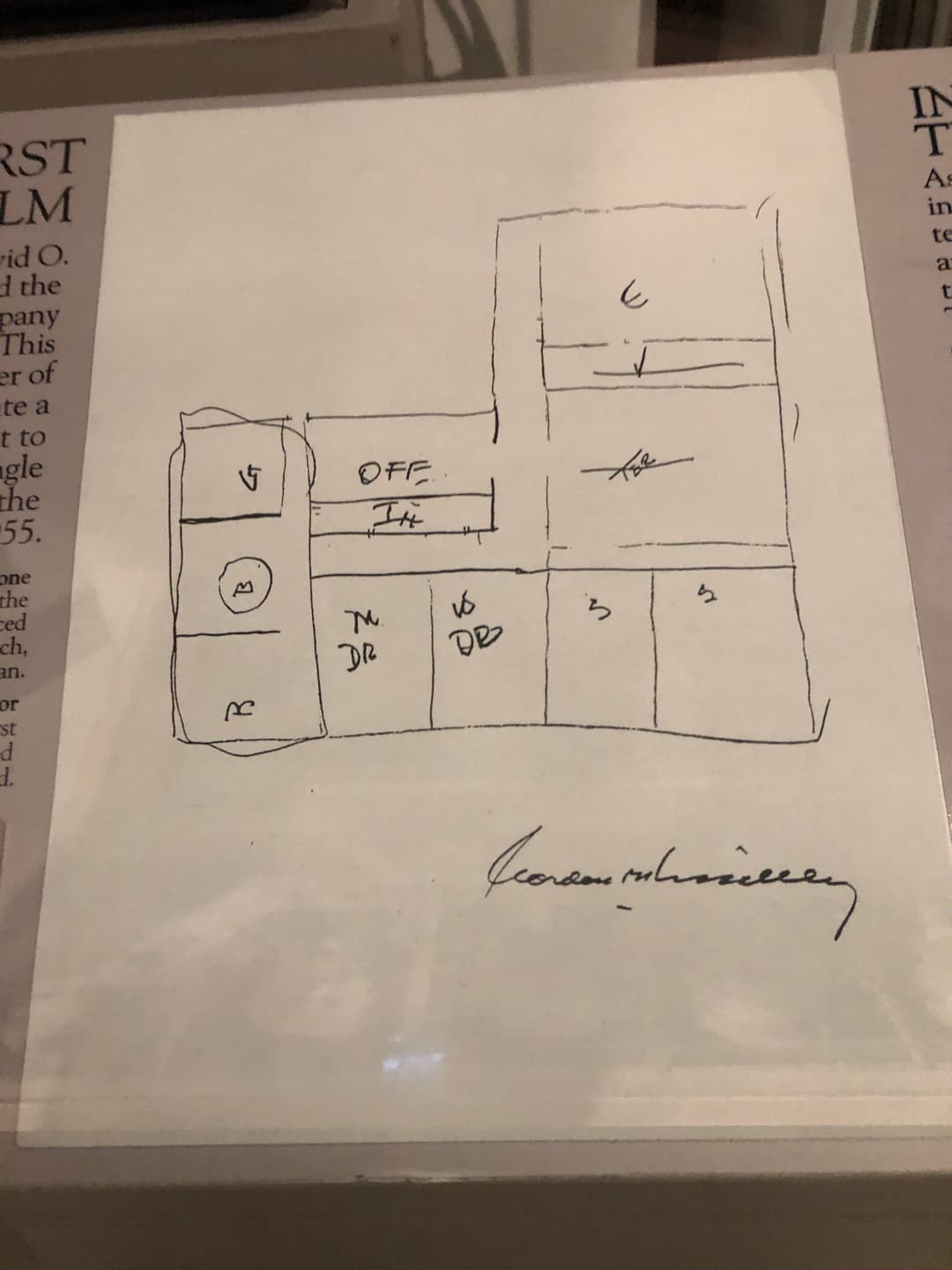 Hand-drawn floor plan with room labels and signature, on display.