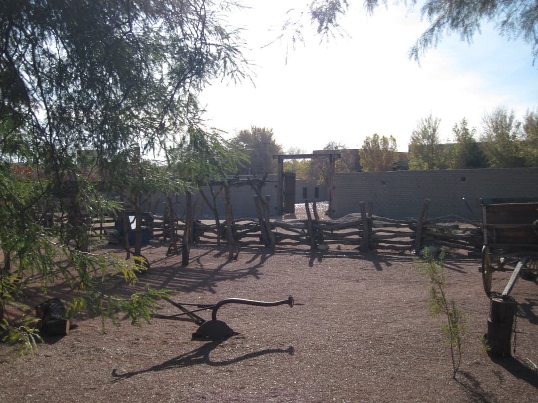 Historic fort grounds featuring a plow, wooden wagon, and rustic fence.