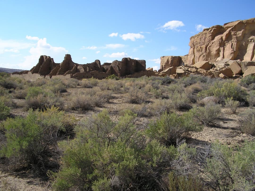 Wide-angle view of Pueblo Bonito ruins and cliff face across desert scrub.