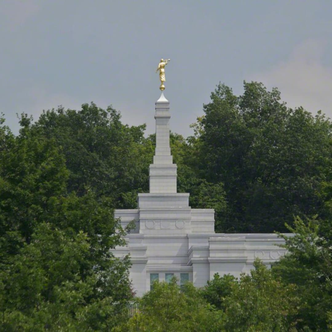 Única aguja del Templo de Palmyra Nueva York con el Ángel Moroni, rodeada de árboles.