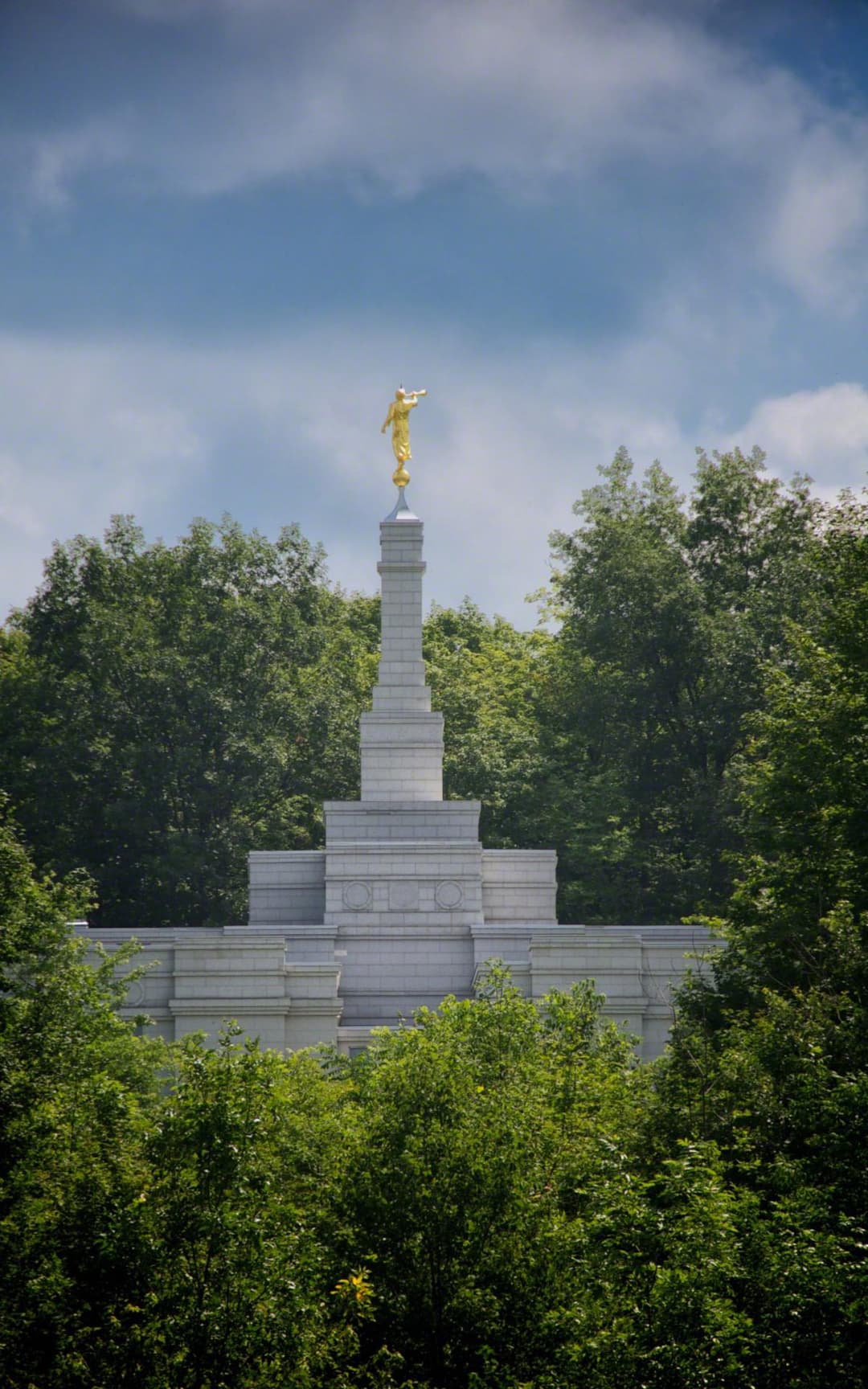 Templo de Palmyra Nueva York, Ángel Moroni en lo alto de la aguja, enmarcado por árboles.