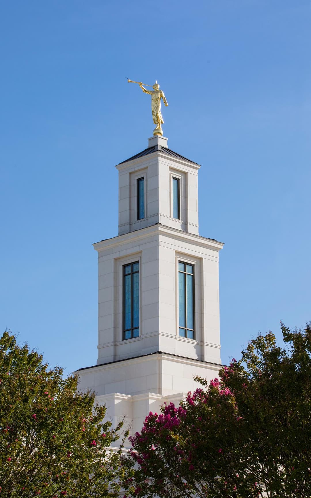 Low-angle view of the spire and Angel Moroni statue against a clear blue sky.