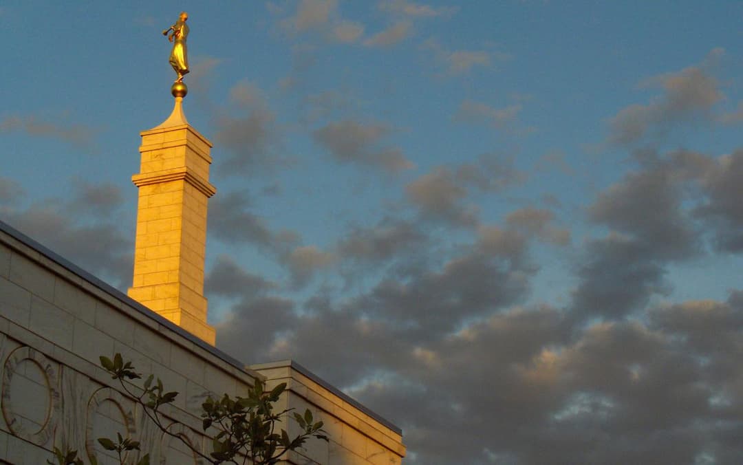 Low-angle view of the single spire and Angel Moroni statue at sunset.