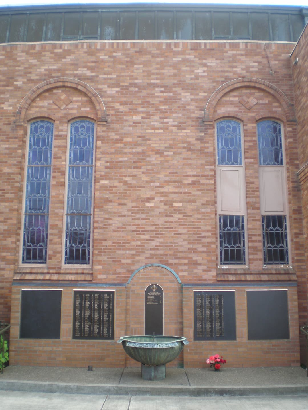 Exterior memorial wall and basin below arched stained-glass windows
