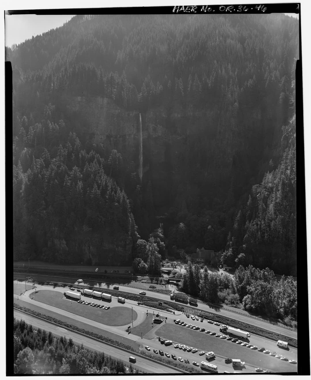 High-angle aerial view of Multnomah Falls, forested cliffs, and parking lot.