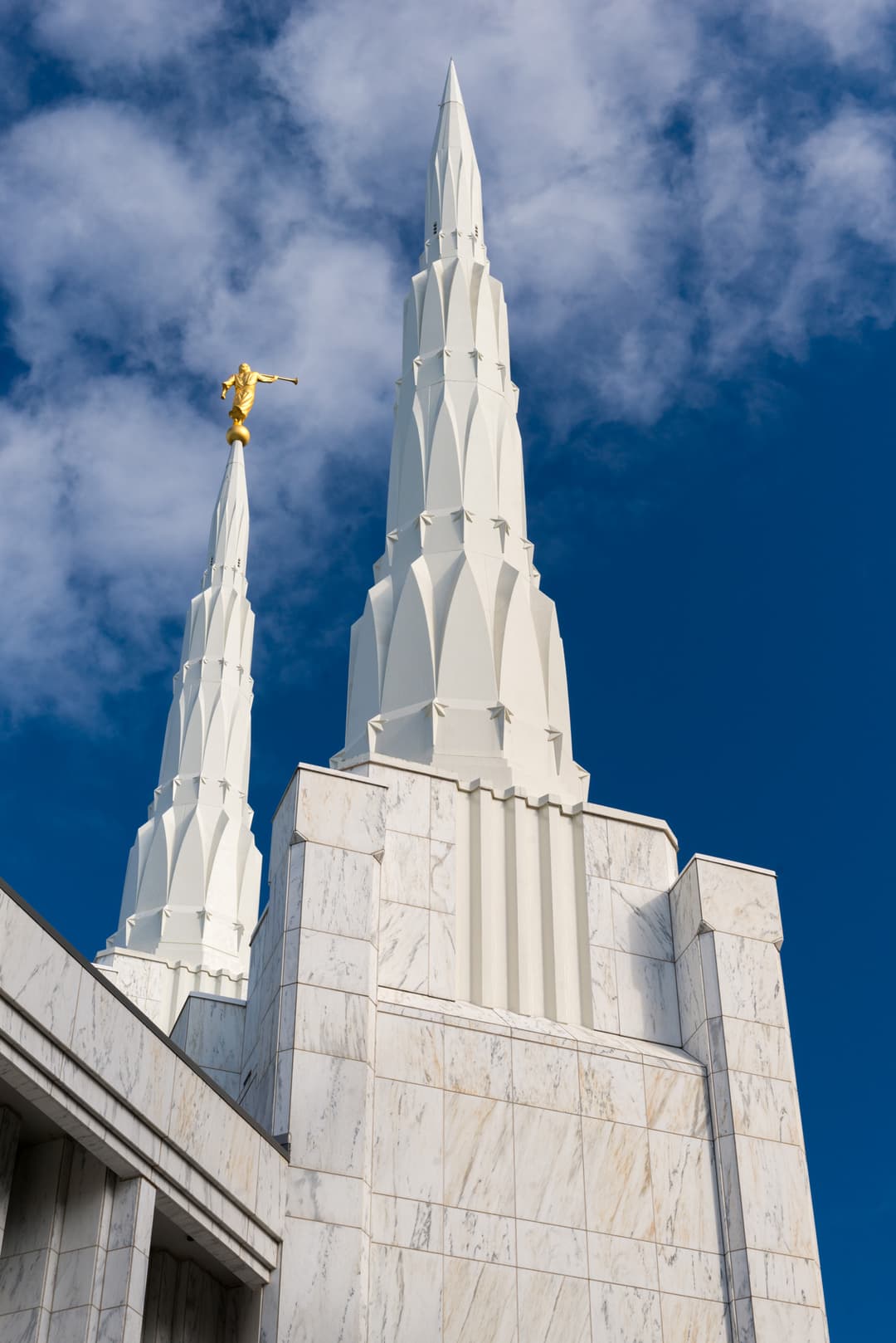 Portland Oregon Temple spires with Angel Moroni statue against a blue sky.