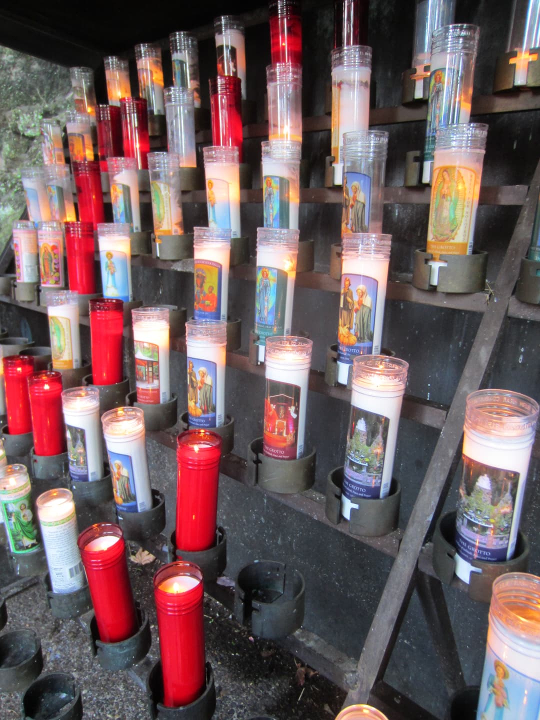 Lit devotional votive candles arranged on tiered racks at The Grotto.