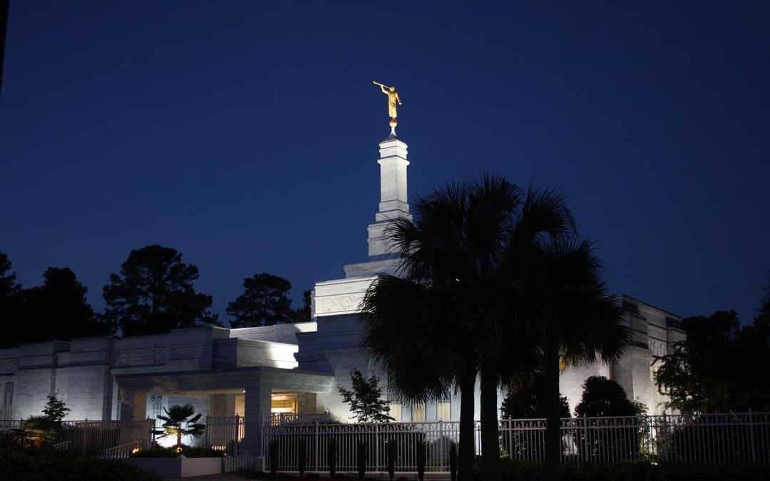 The Columbia South Carolina Temple illuminated at twilight with palm trees.