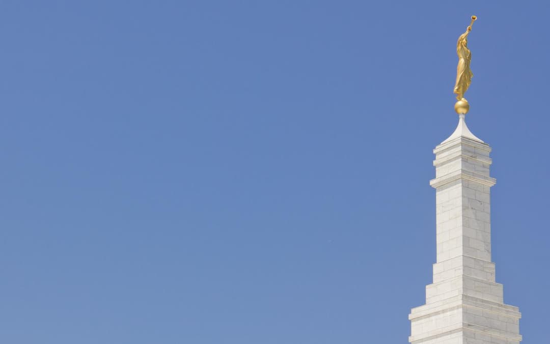 The temple spire and golden Angel Moroni statue against a clear blue sky.