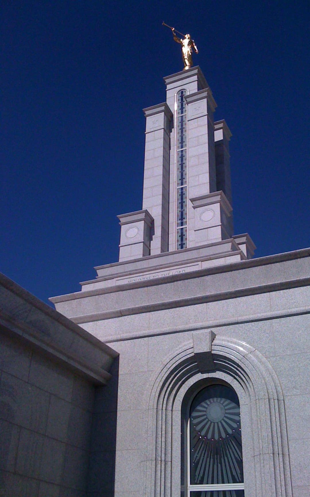 Lubbock Texas Temple tower, Angel Moroni, and sunburst window against blue sky.