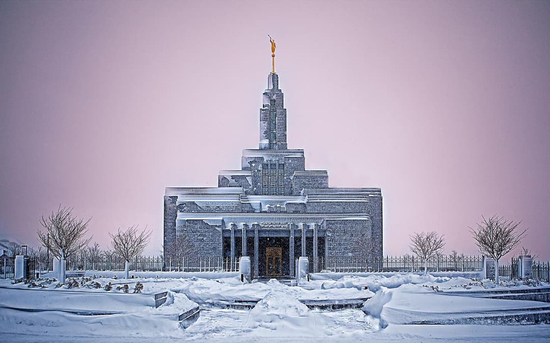 Draper Utah Temple, frontal view, covered in snow under a pink sky.