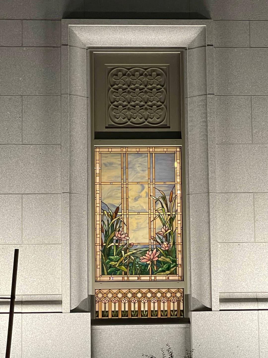 Exterior detail of a stained glass window featuring local wetland vegetation.