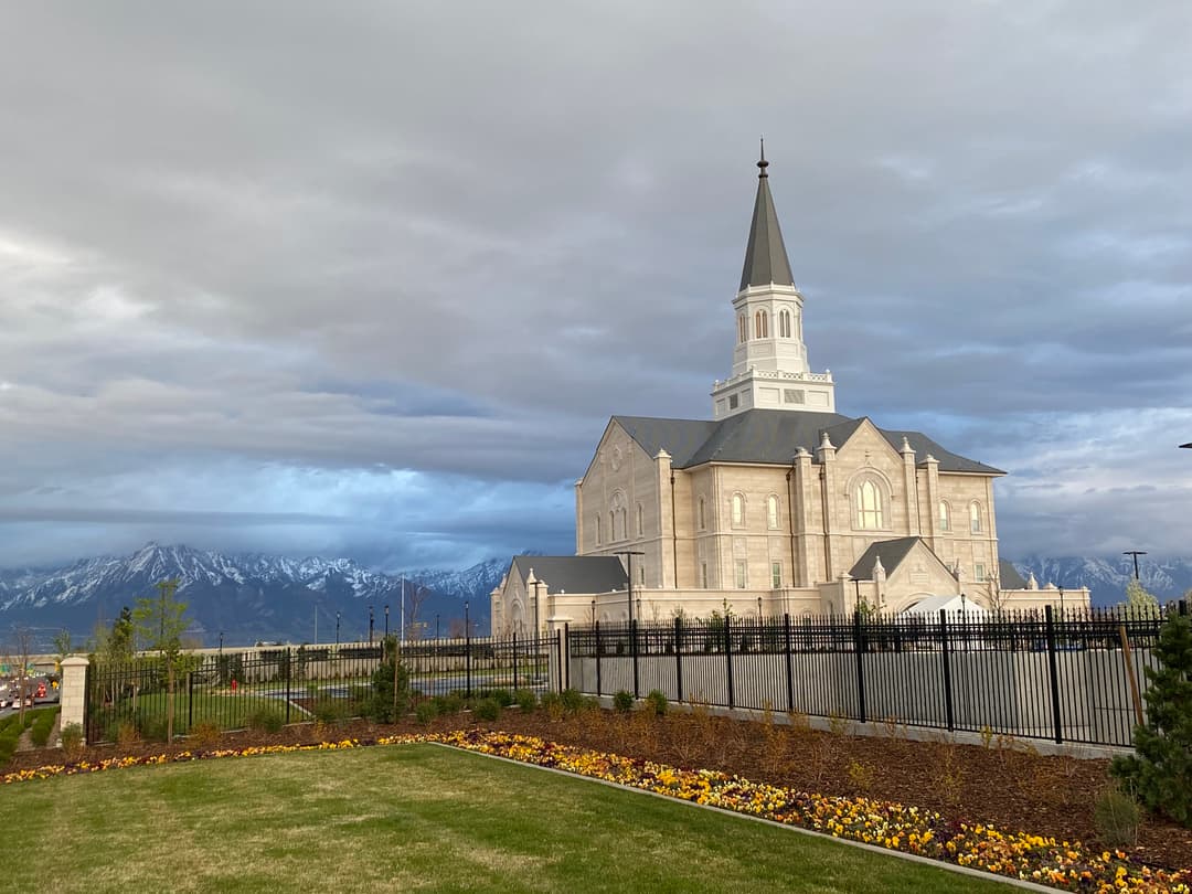 Exterior view of Taylorsville Utah Temple with flowerbeds and mountains.