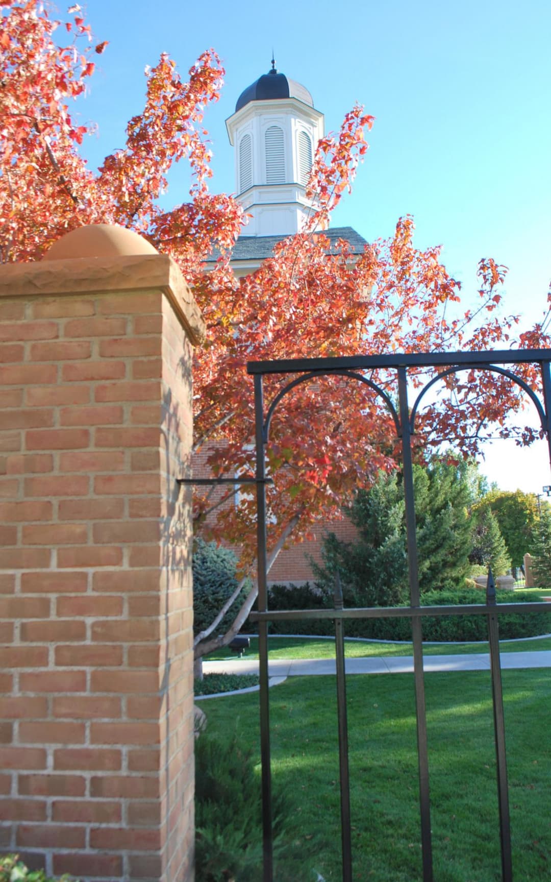 Vernal Utah Temple cupola framed by autumn trees and a brick pillar.