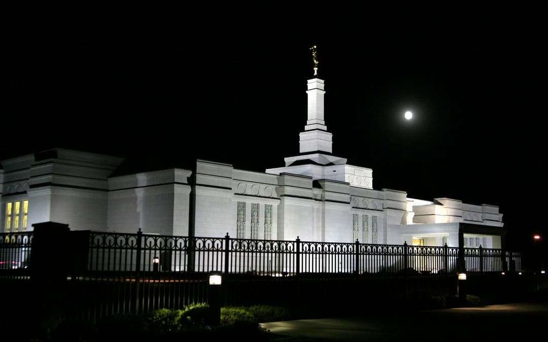 The Spokane Washington Temple illuminated at night beneath a full moon.
